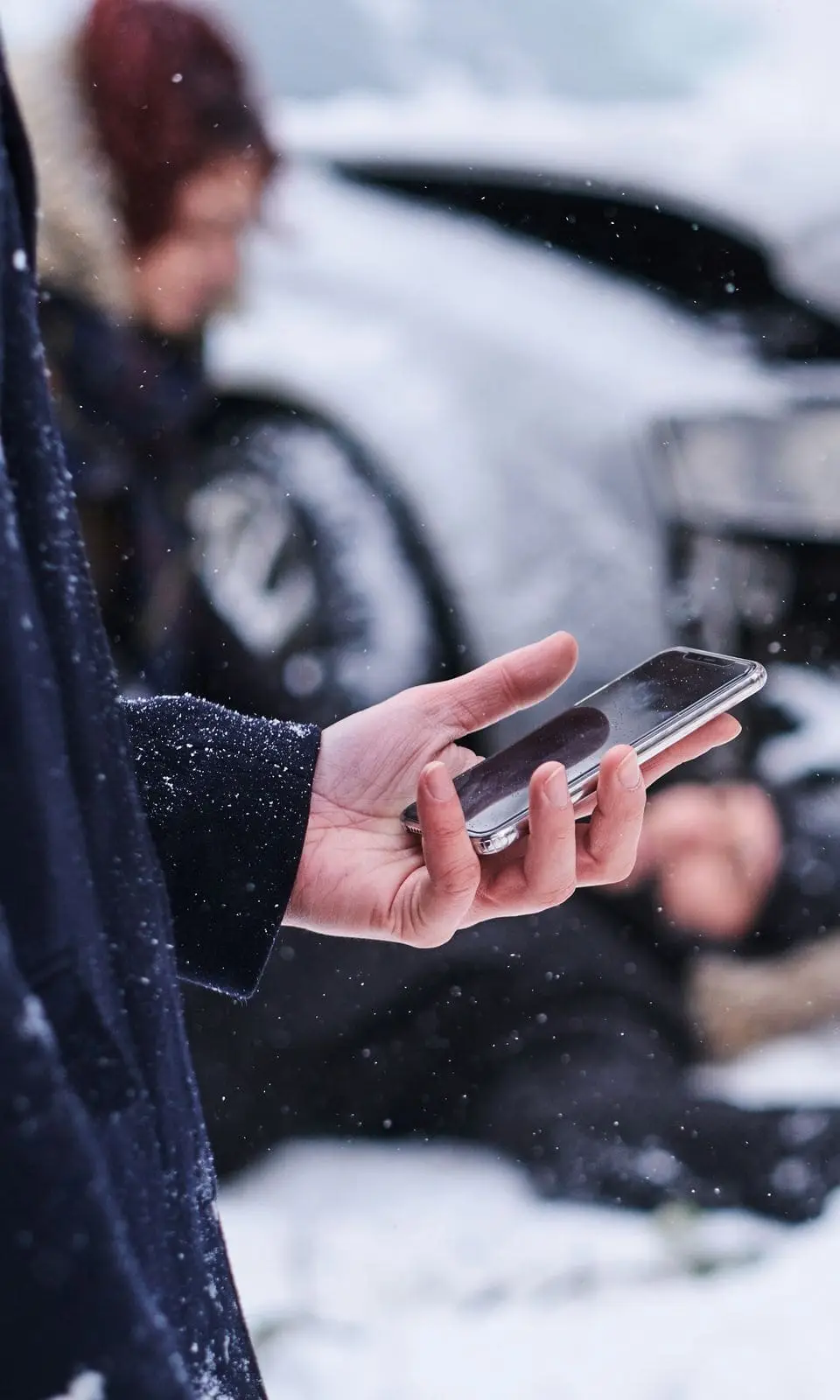 Persona pidiendo ayuda con el celular junto a un auto chocado en una calle nevada