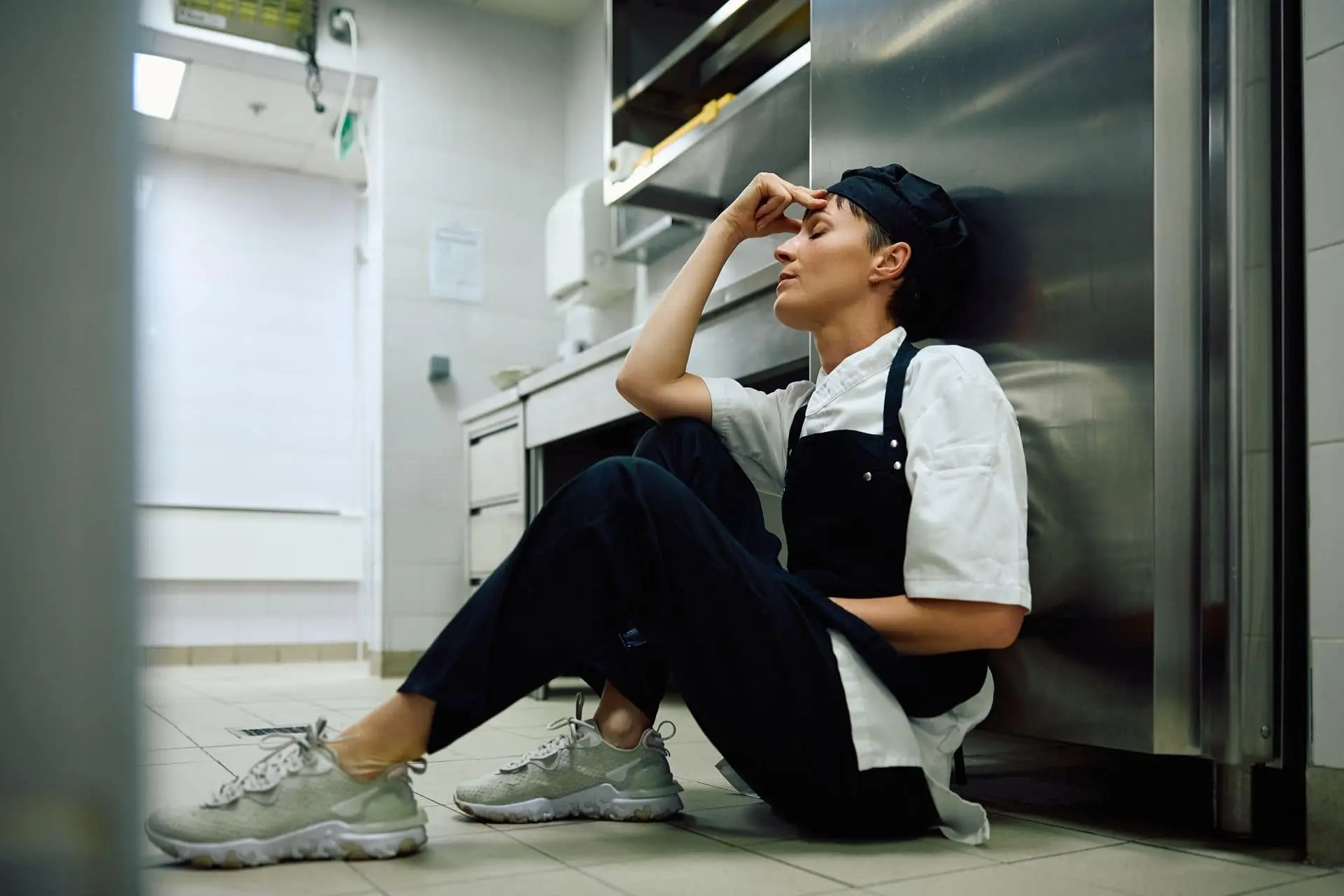 Cocinera sentada en el piso de la cocina, con dolor, durante su jornada