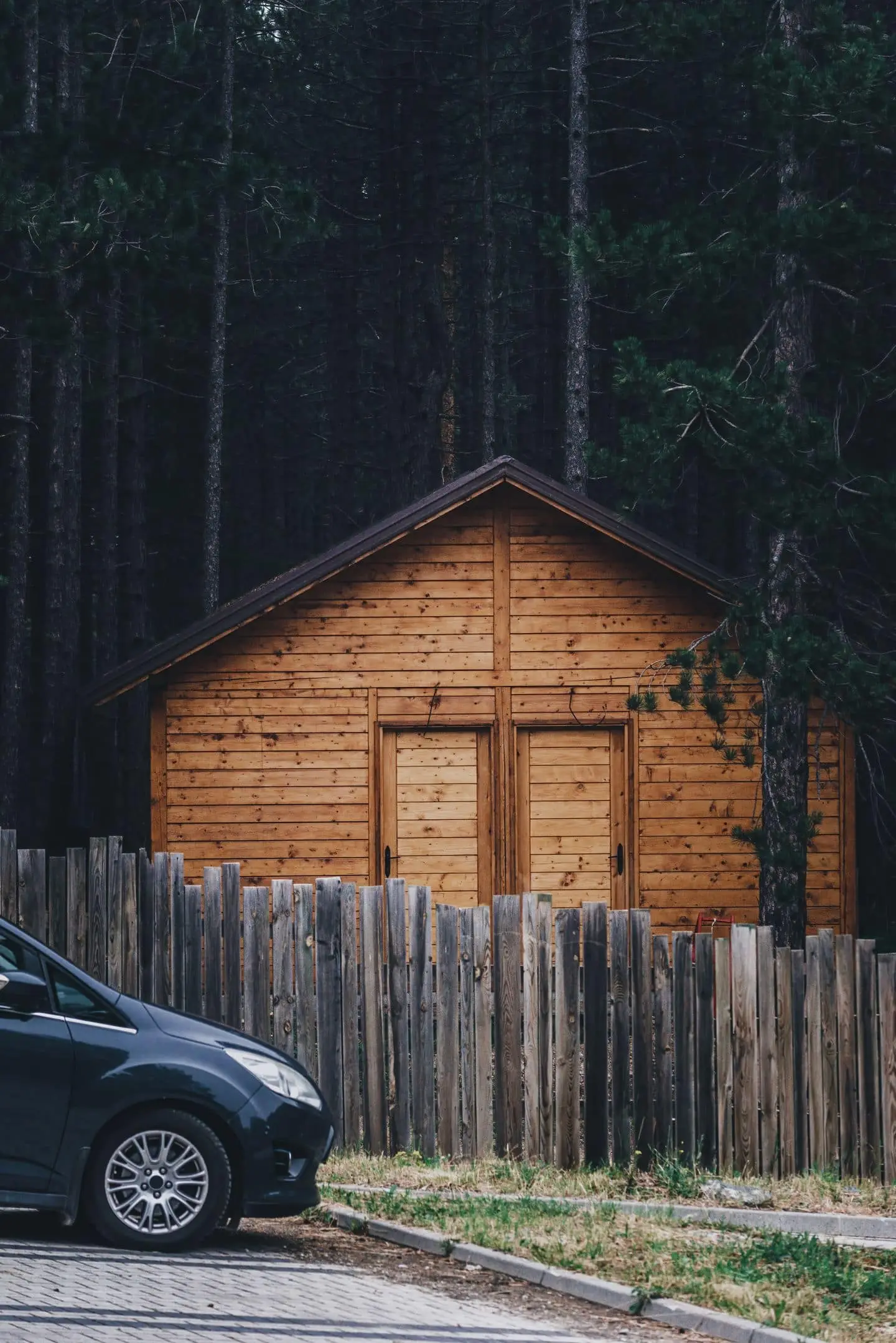 Casa de madera en el bosque con un auto estacionado frente a la cerca
